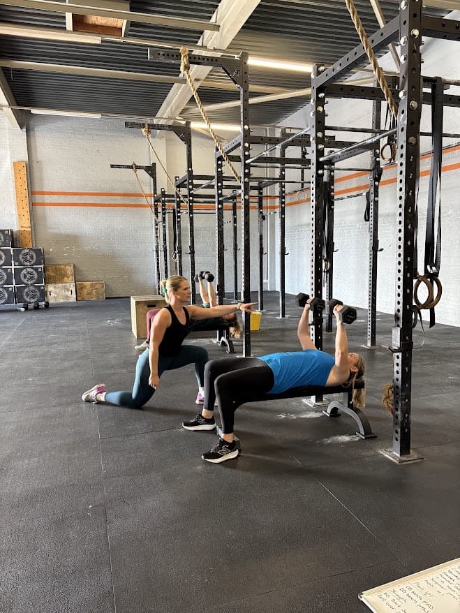 Kate coaching a client through a dumbbell bench press at Forged Gym